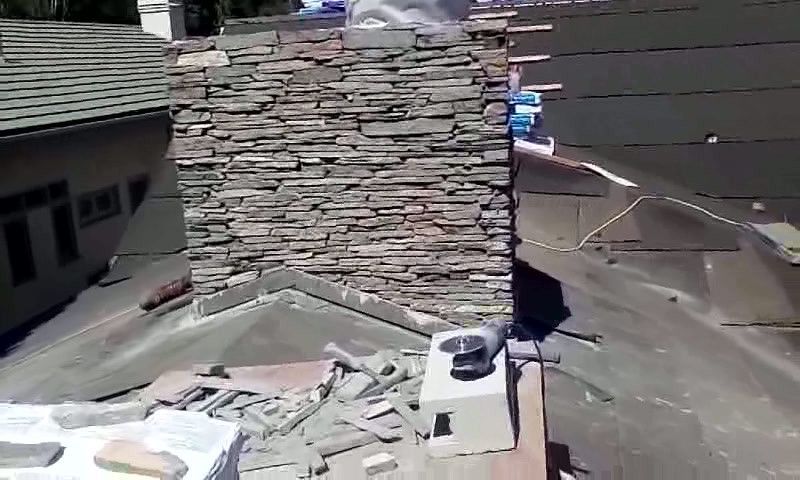 Rooftop with a stone chimney, scattered roofing materials, and a black cat near the chimney.