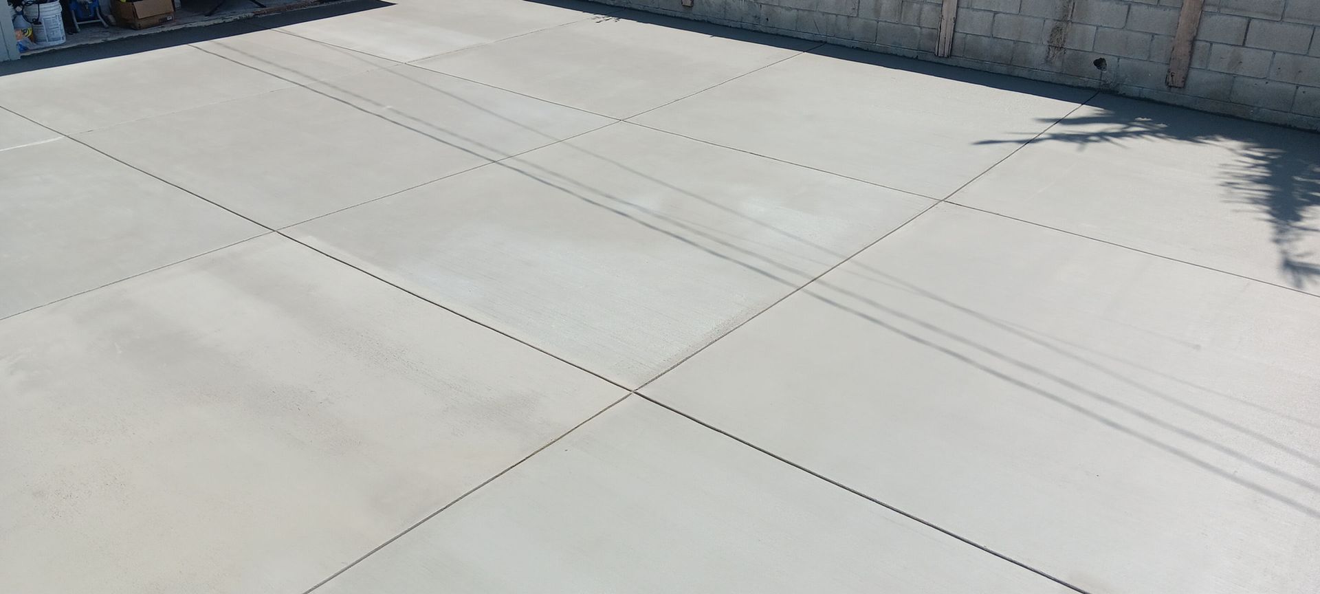 Empty concrete driveway with expansion joints beside a brick wall in bright sunlight