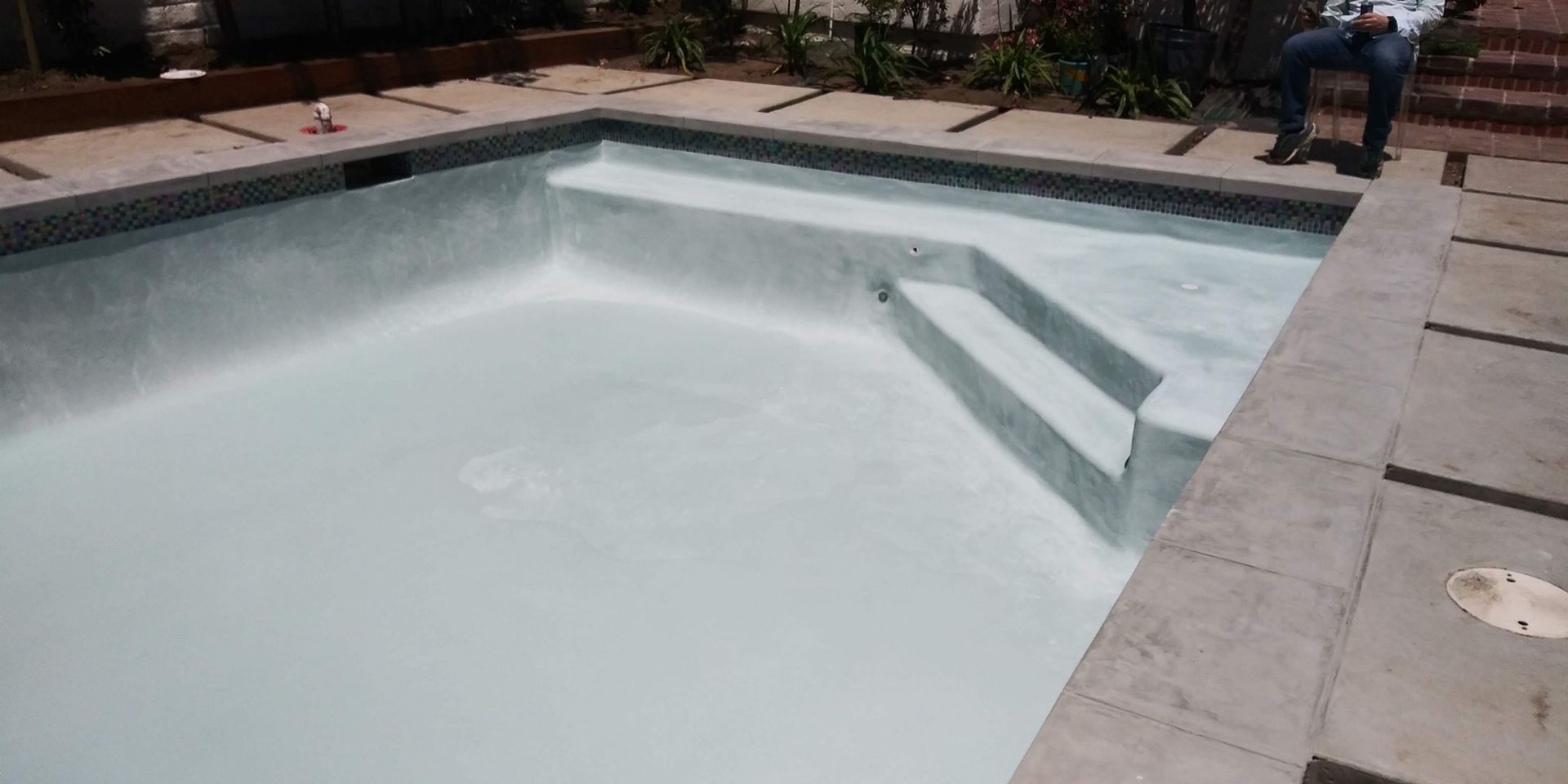 Empty backyard swimming pool with steps and a concrete deck around it