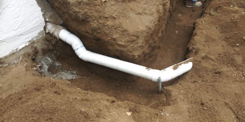 White pipe laid across a dirt trench beside a rocky excavation site.