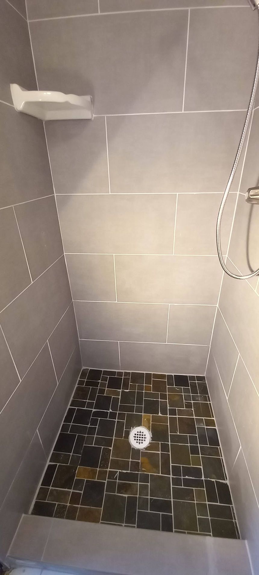 Small tiled shower stall with a dark mosaic floor and wall shelf.