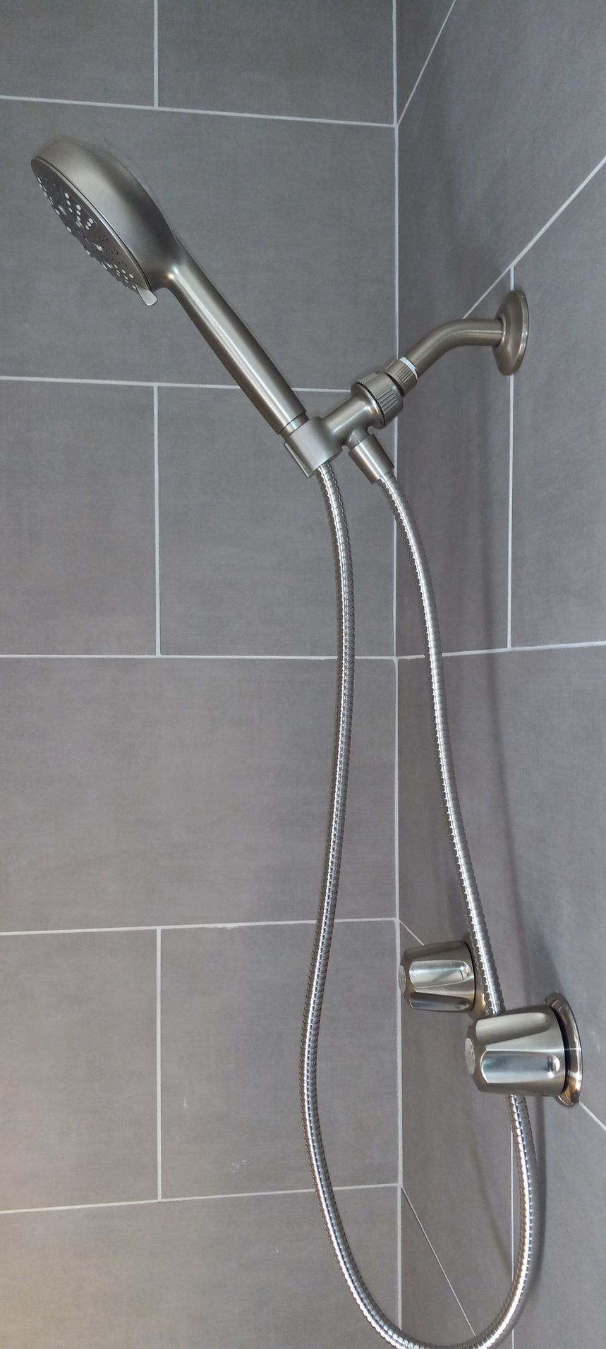 Handheld showerhead with hose mounted on a gray tiled bathroom wall