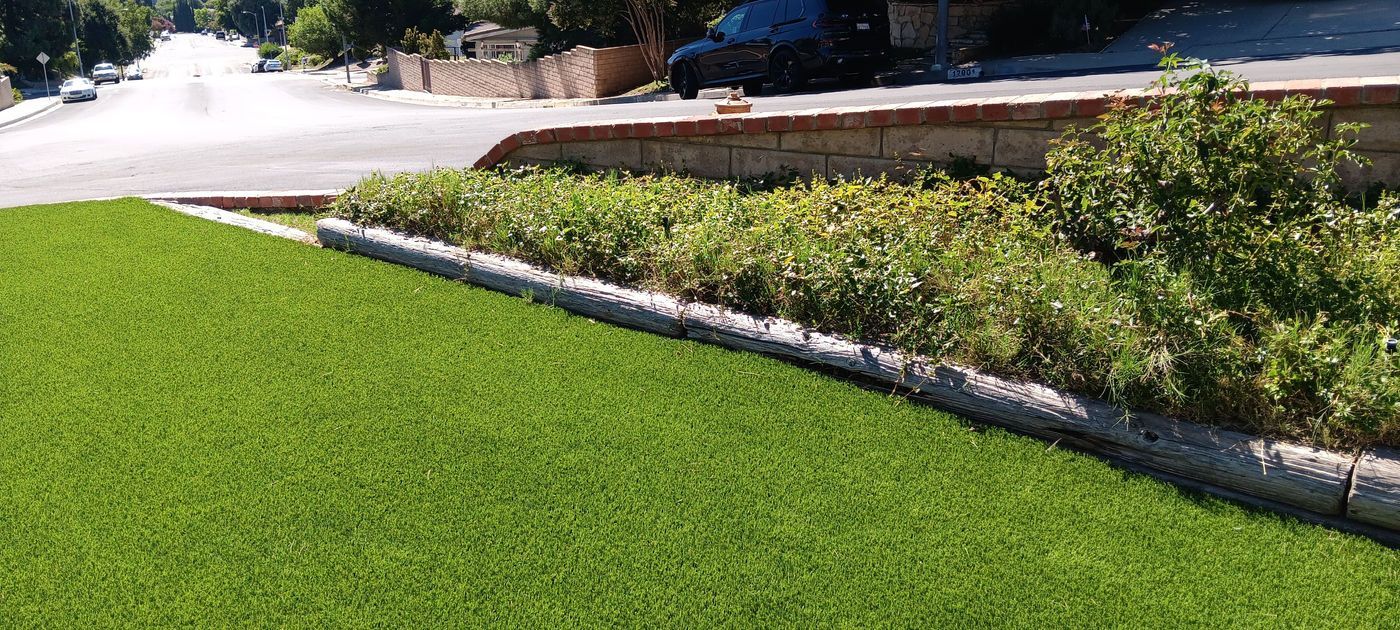 Bright green lawn beside a landscaped flowerbed and paved path in a sunny outdoor area