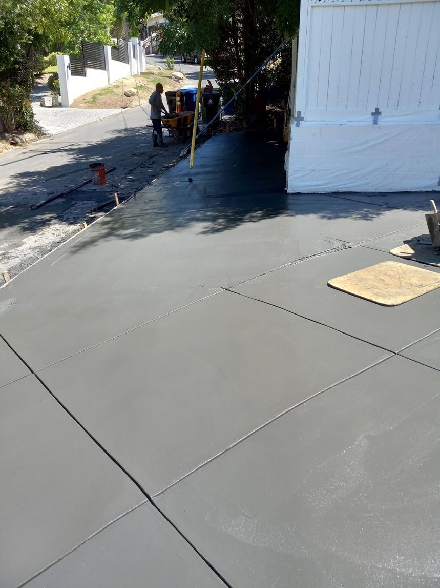 Concrete driveway beside a white garage, with two workers near the street and a sidewalk to the left.