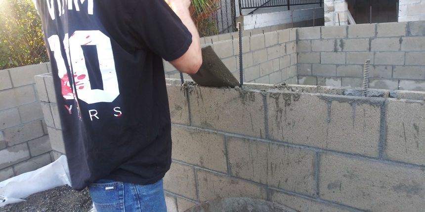 Person in black shirt standing beside a cinder block wall under construction