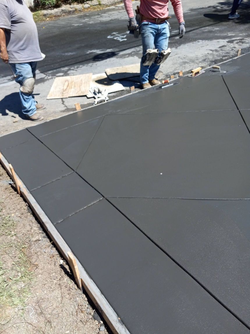Freshly paved black concrete sidewalk with two workers nearby and tools on the ground