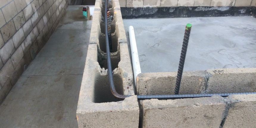 Concrete block foundation with protruding pipes and rebar in a construction area
