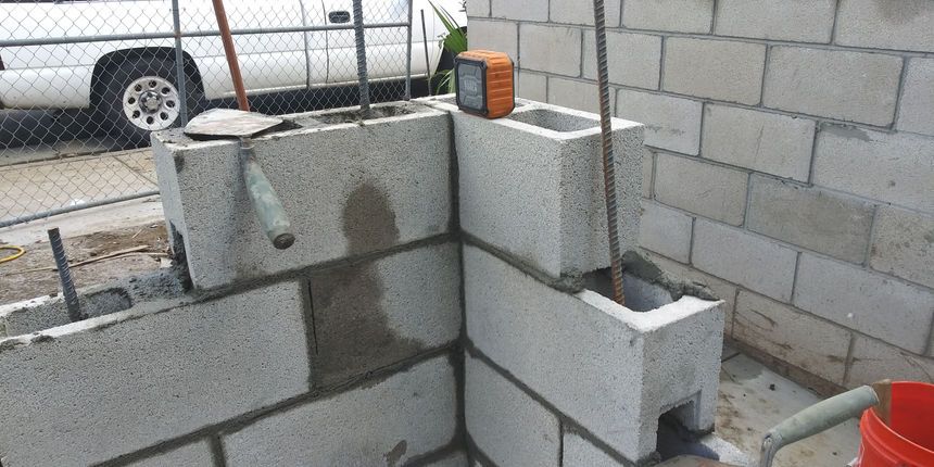 Cinder blocks and concrete blocks stacked near a cinder block wall, with a ladder in the background.