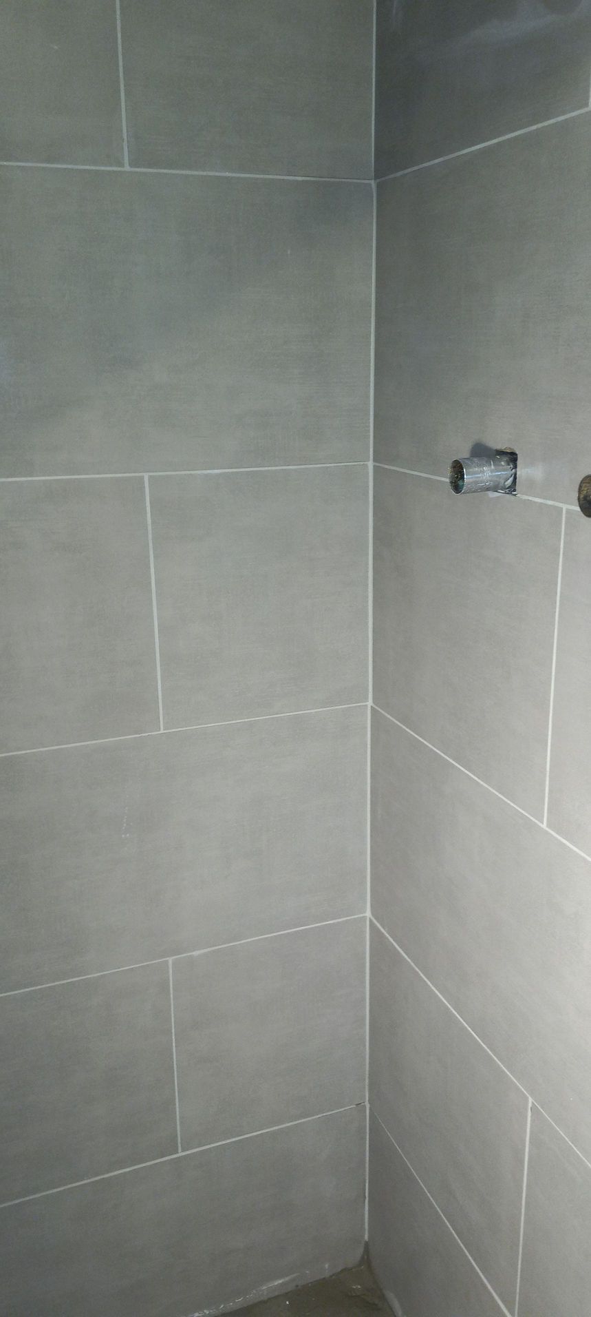 Gray tiled shower corner with plumbing fixtures and a bare floor opening