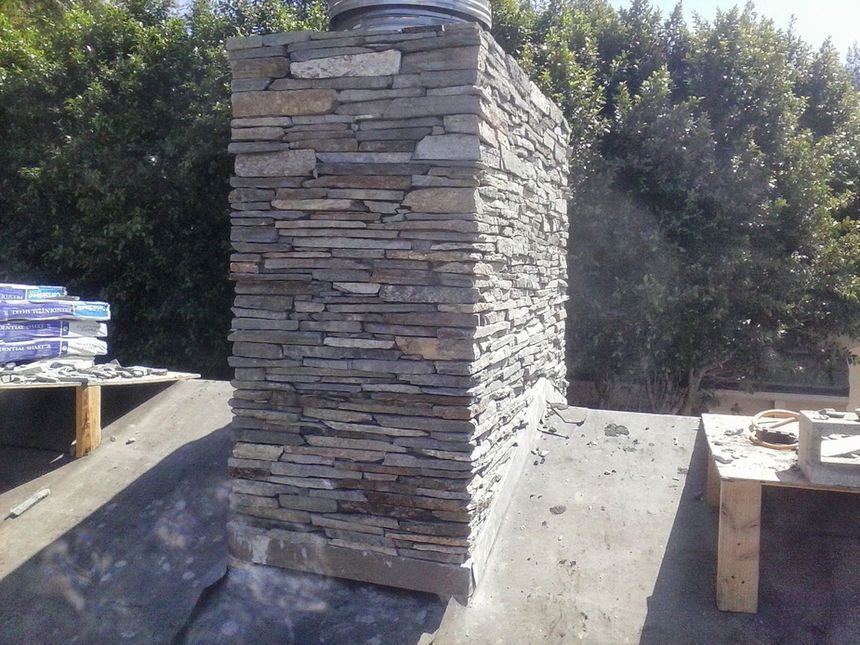 Stacked stone wall section on a rooftop with lumber and materials nearby, outdoors in sunlight
