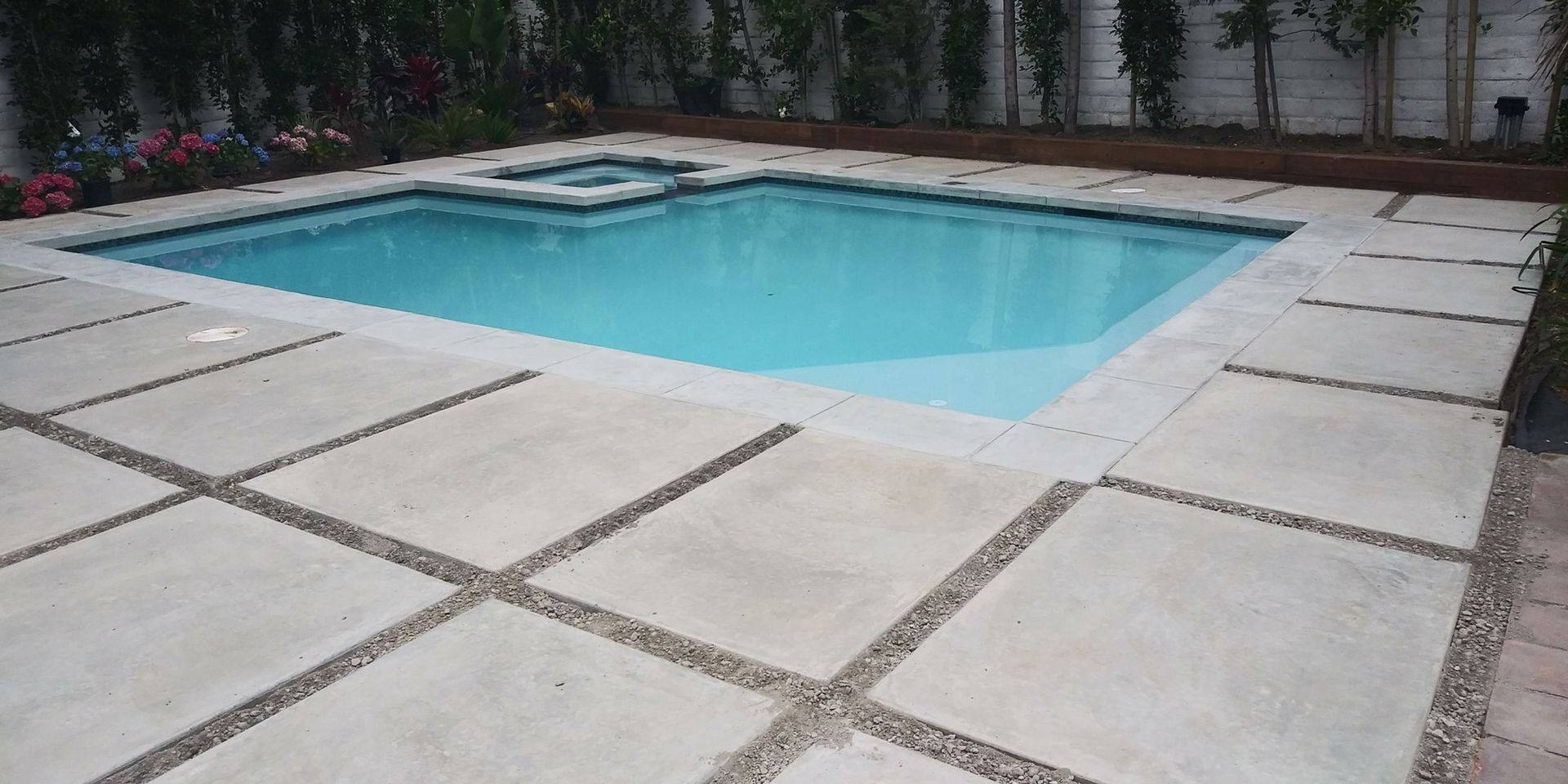 Rectangular backyard swimming pool with turquoise water, surrounded by large stone patio tiles and trees.