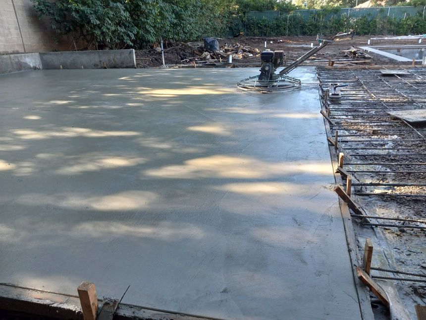 Freshly poured concrete slab at a construction site with rebar and wooden forms along the edge
