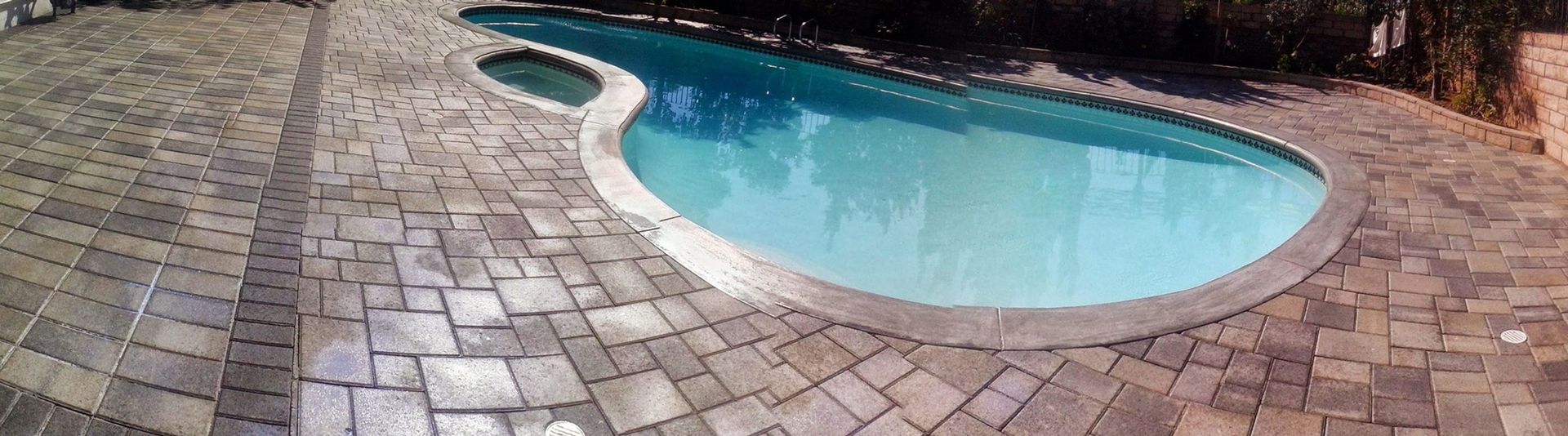 Curved backyard swimming pool with light blue water and stone patio paving
