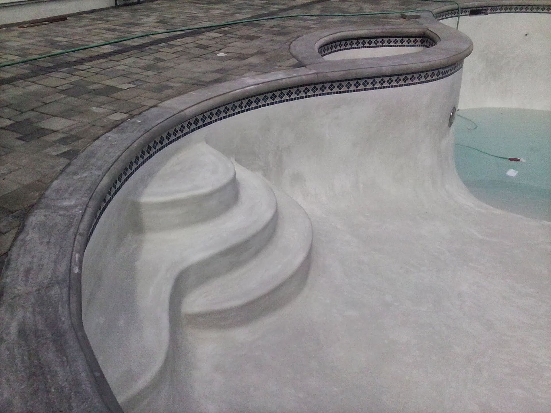 Empty concrete swimming pool with steps and a curved edge, viewed from above.