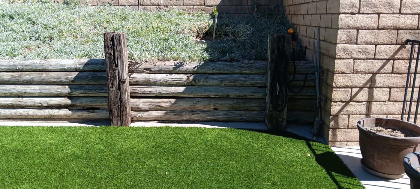 Backyard patio with green lawn, wooden fence, stone wall, and a potted planter at right