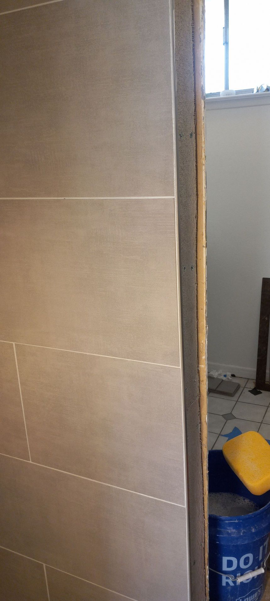Partially tiled wall beside a doorway, with a blue bucket and yellow sponge in a small room