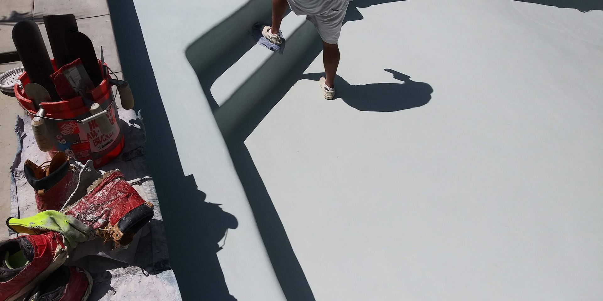Person in gray walks on a rooftop near red equipment and long shadows.