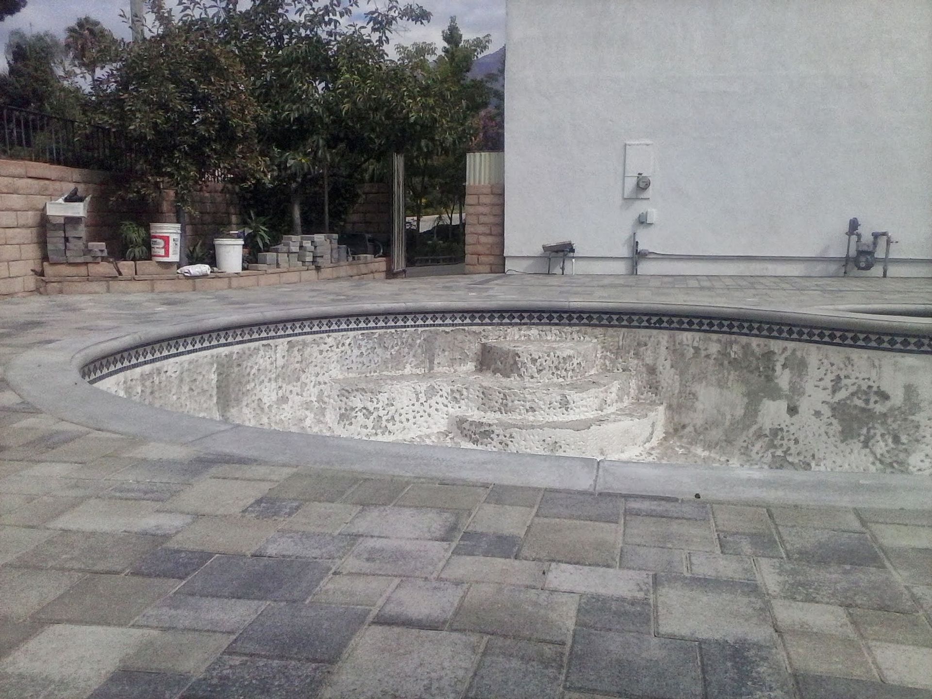Empty drained pool beside a tiled patio and white wall