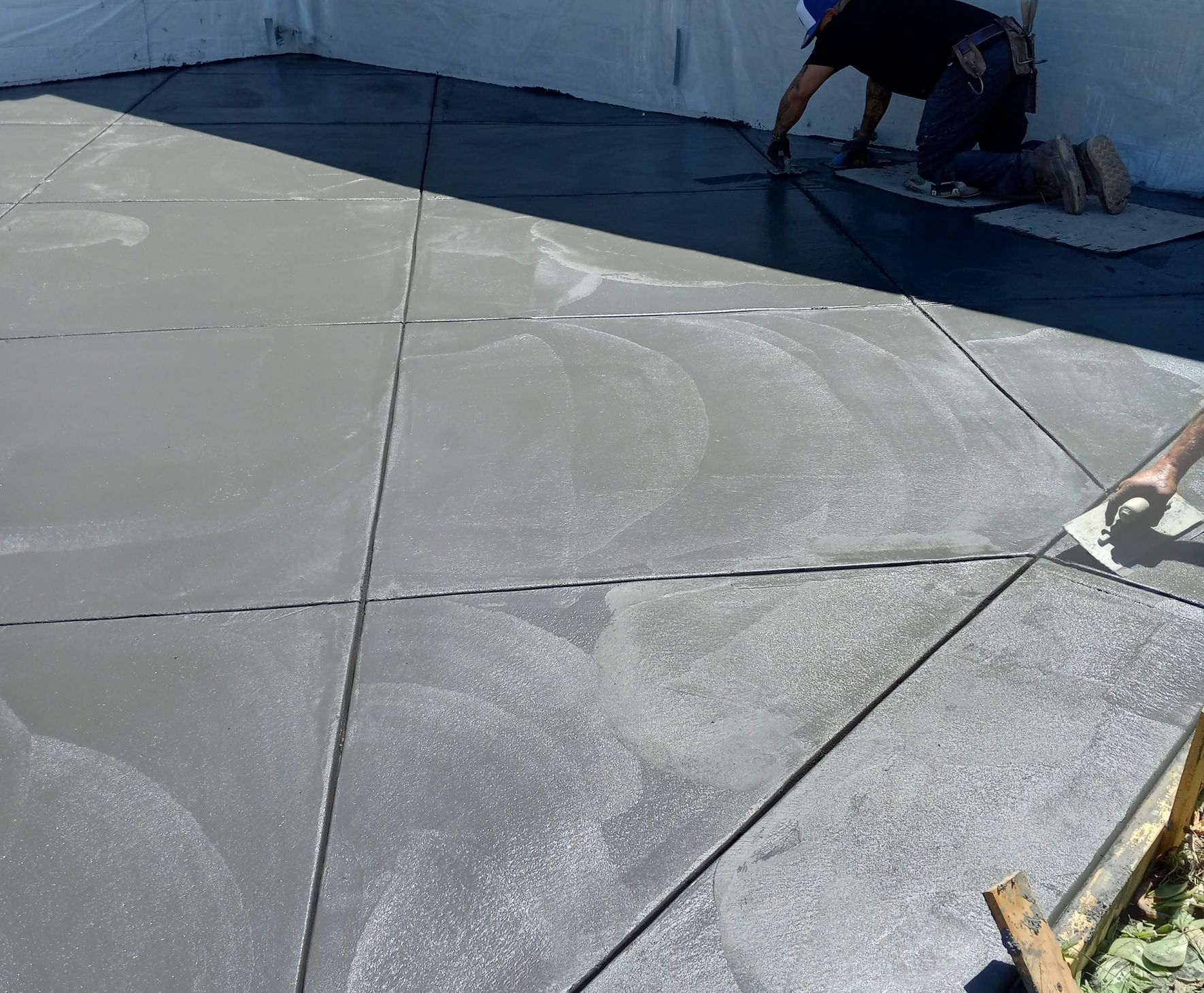 Workers applying white coating to a flat rooftop surface with visible seams and a dark border