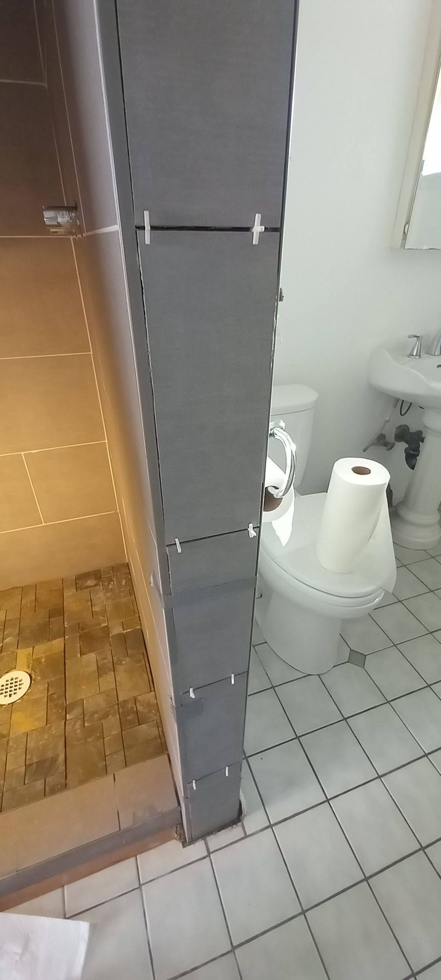 Small bathroom with tiled floor, toilet, and white toilet paper roll holder beside a shower stall.