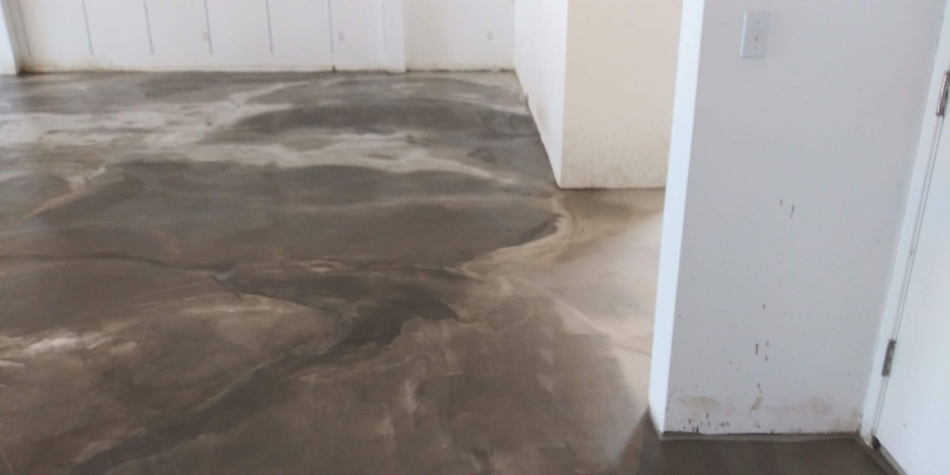 Empty room with wet, uneven concrete floor and white walls near a doorway