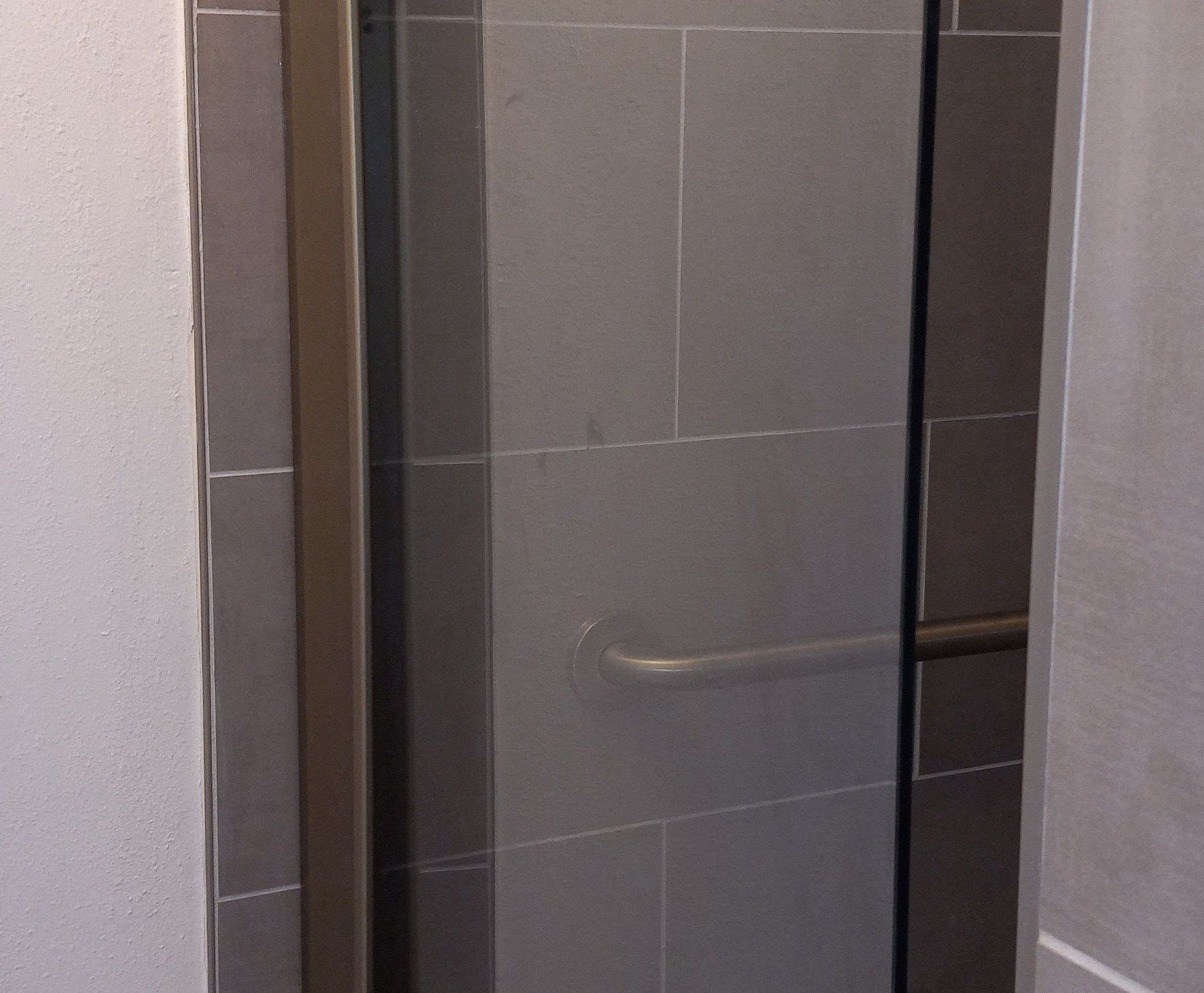 Glass shower door with a chrome grab bar in a tiled bathroom