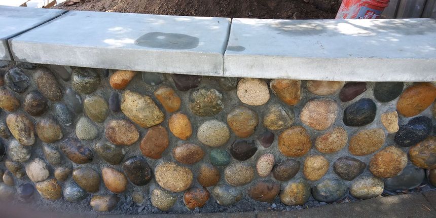 Curved stone wall with rounded river rocks and a light gray concrete cap