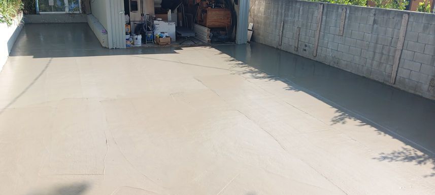 Empty concrete driveway beside a garage and tall fence in bright sunlight