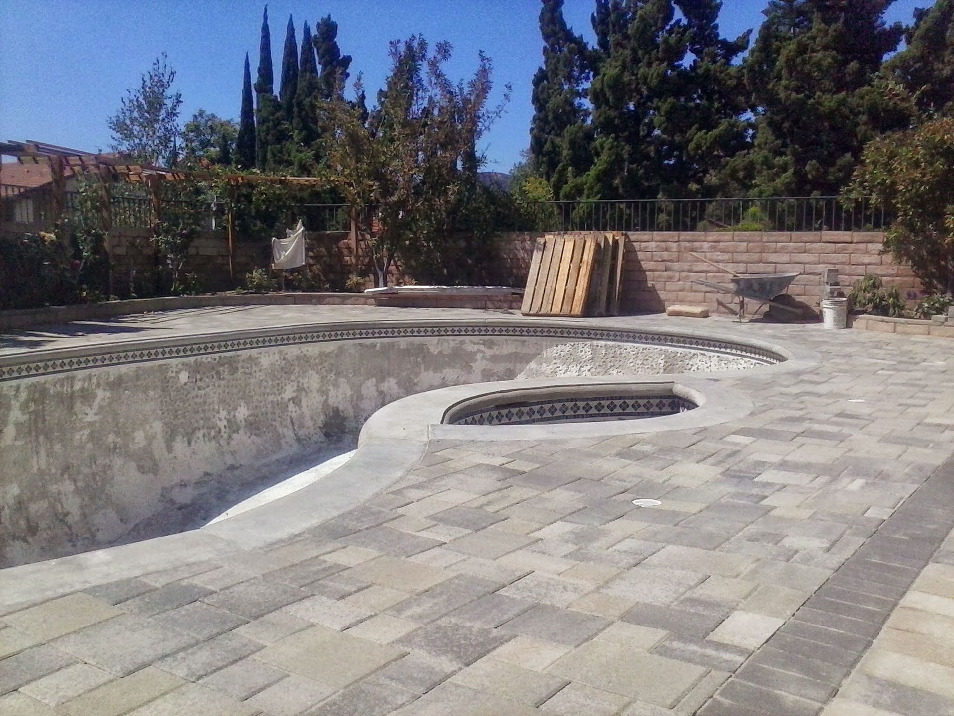 Empty concrete backyard pool under construction with a circular drain opening and stacked lumber nearby