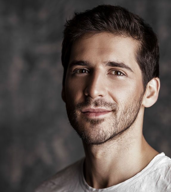 Studio portrait of a smiling man with dark hair against a blurred gray background
