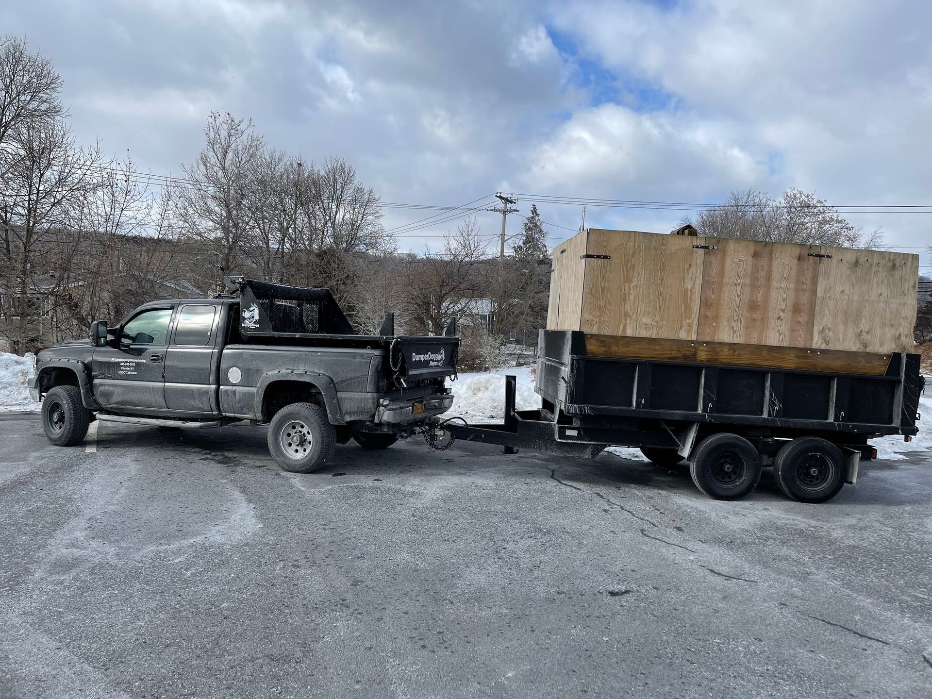 Pickup truck towing a black trailer loaded with a large wooden crate in a gravel lot