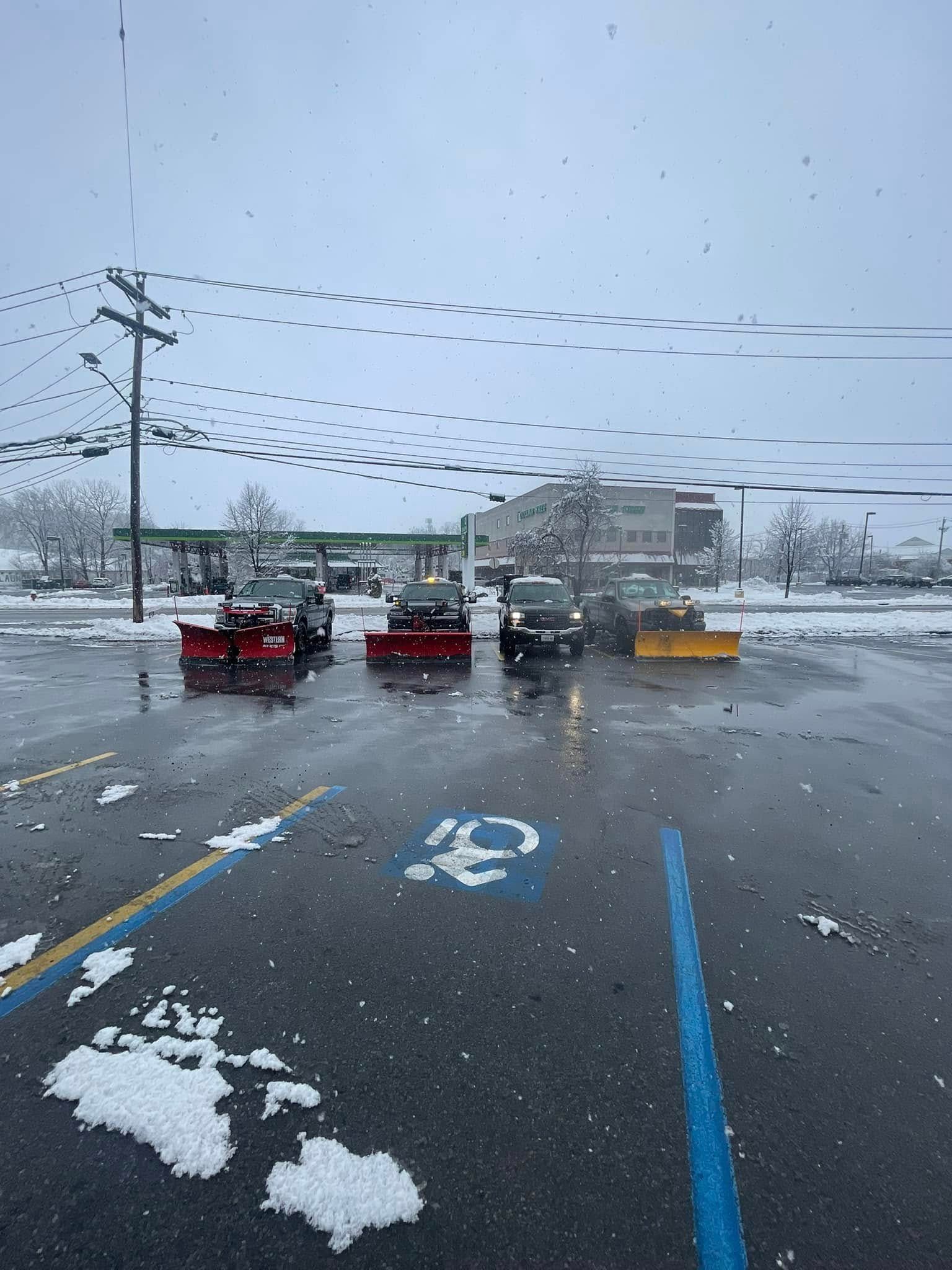 Snowy parking lot with several cars and blue handicapped spaces under a cloudy sky
