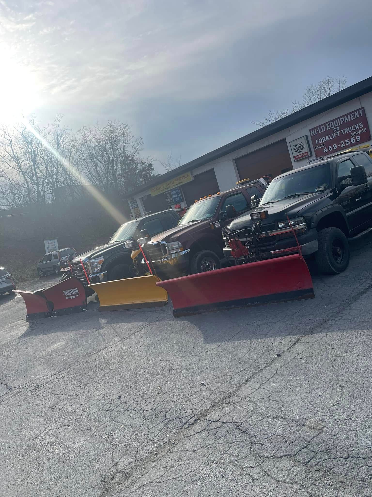 Two off-road utility vehicles parked behind red and yellow snow plows in a sunny lot