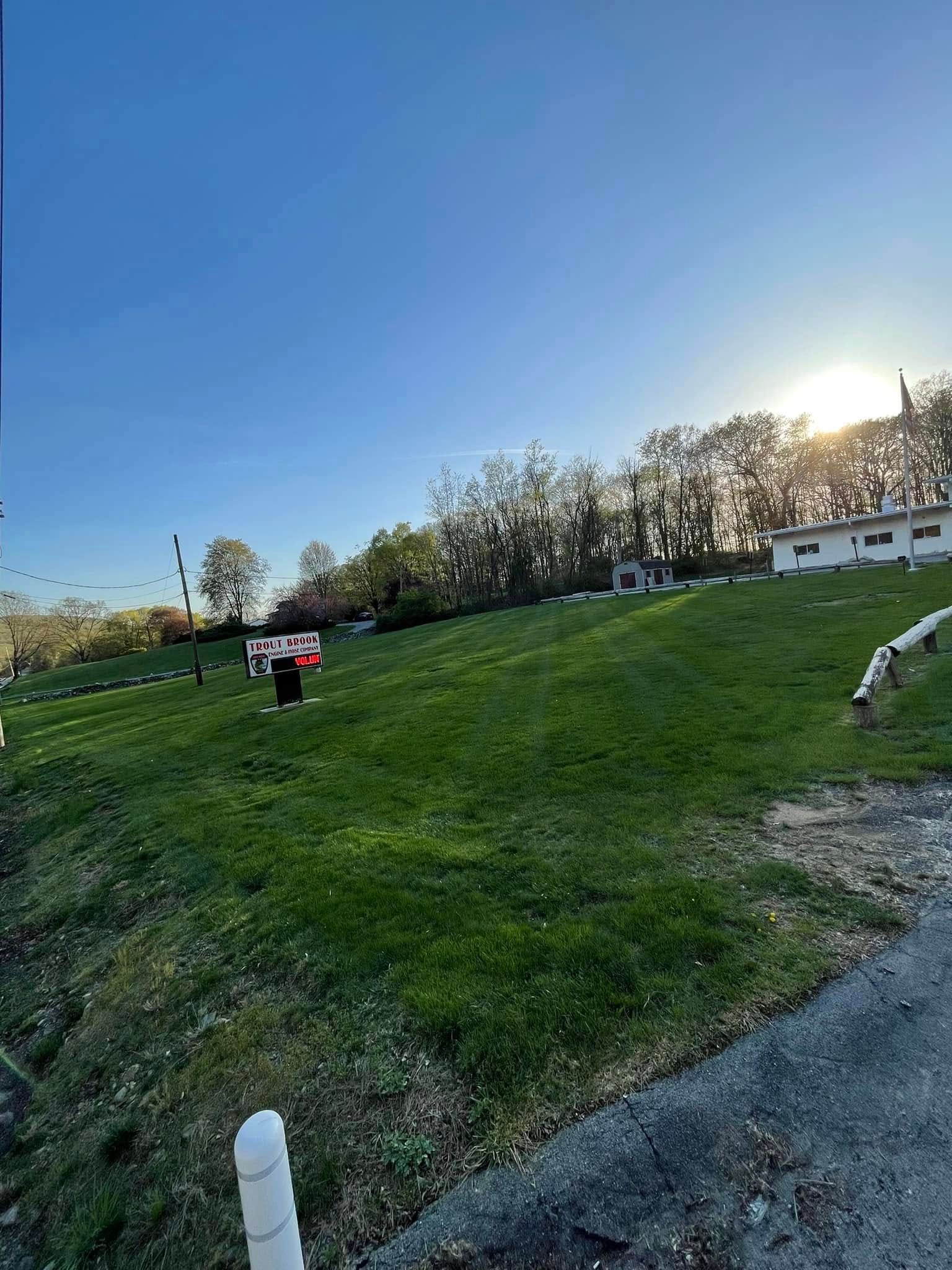 People walking on a grassy hill at sunset near houses and trees.