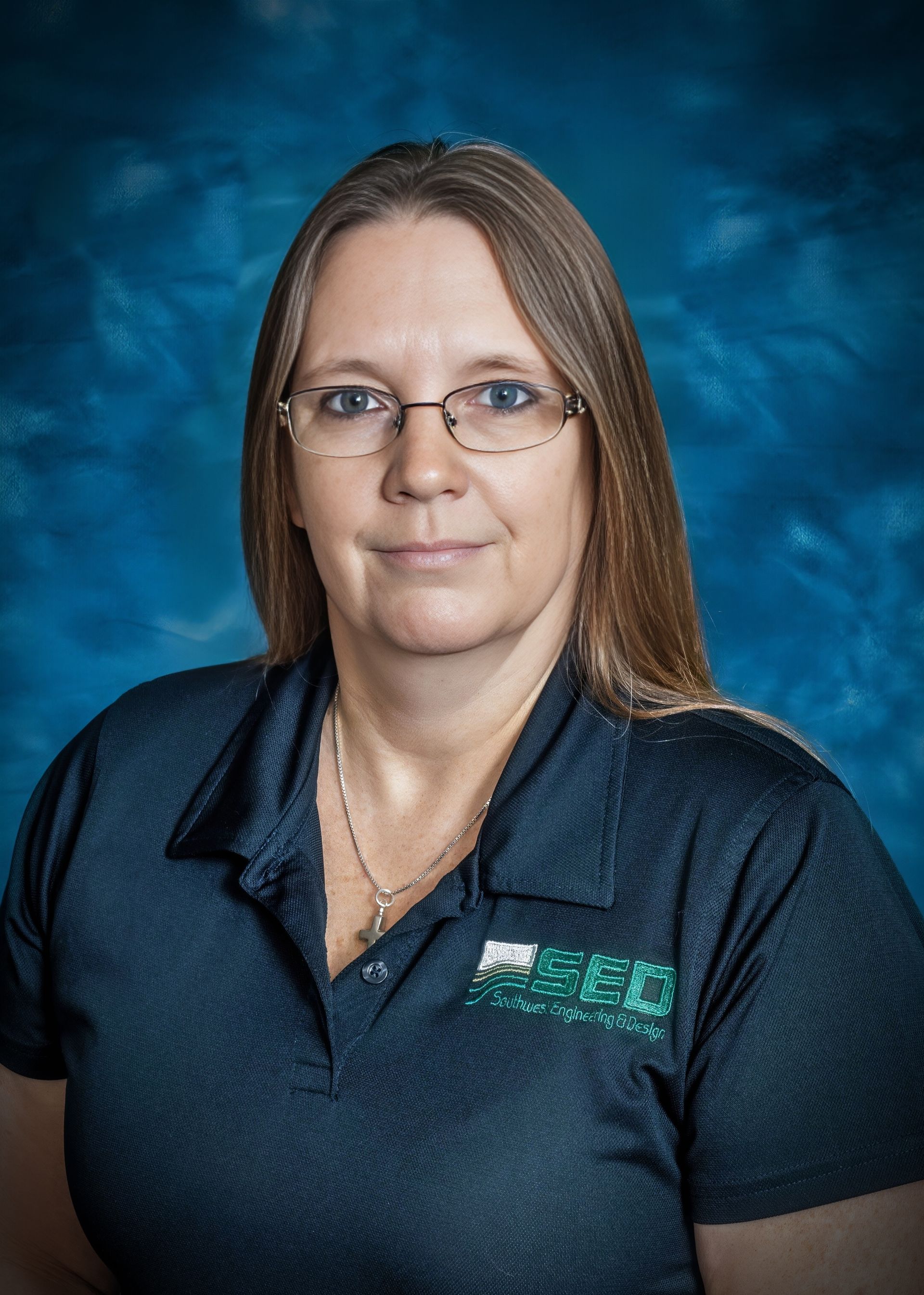 Woman with glasses, light brown hair, wearing a dark blue polo shirt, blue background.