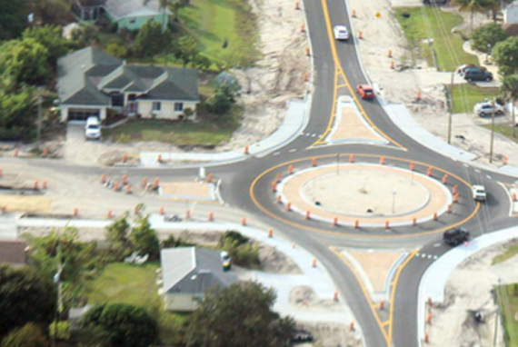 Aerial view of a newly constructed roundabout with cars, orange cones, and residential houses.