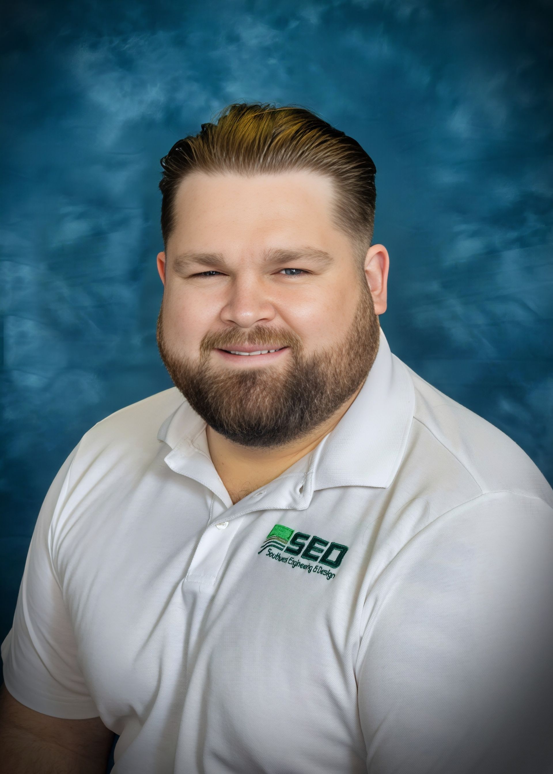 Man with beard, smiling, wearing white polo shirt with 