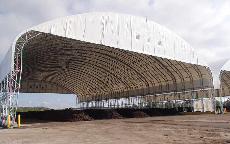Large white fabric-covered composting building, holding a long pile of dark compost in an open space.