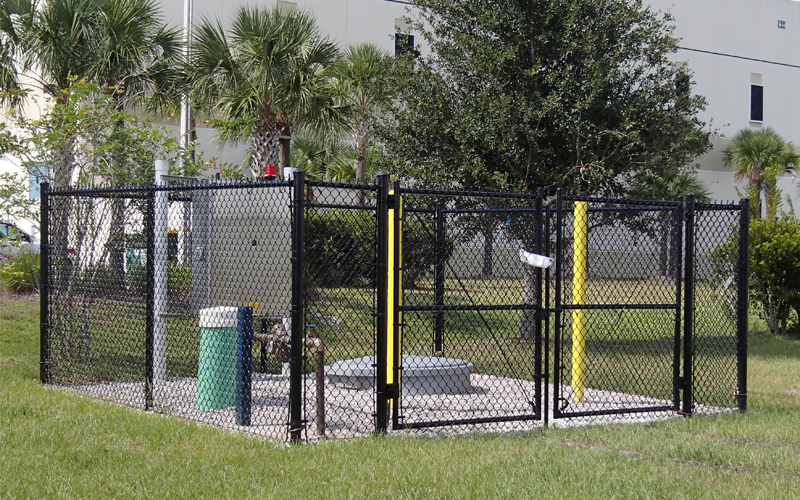 Black fenced enclosure with equipment, grass, and trees.