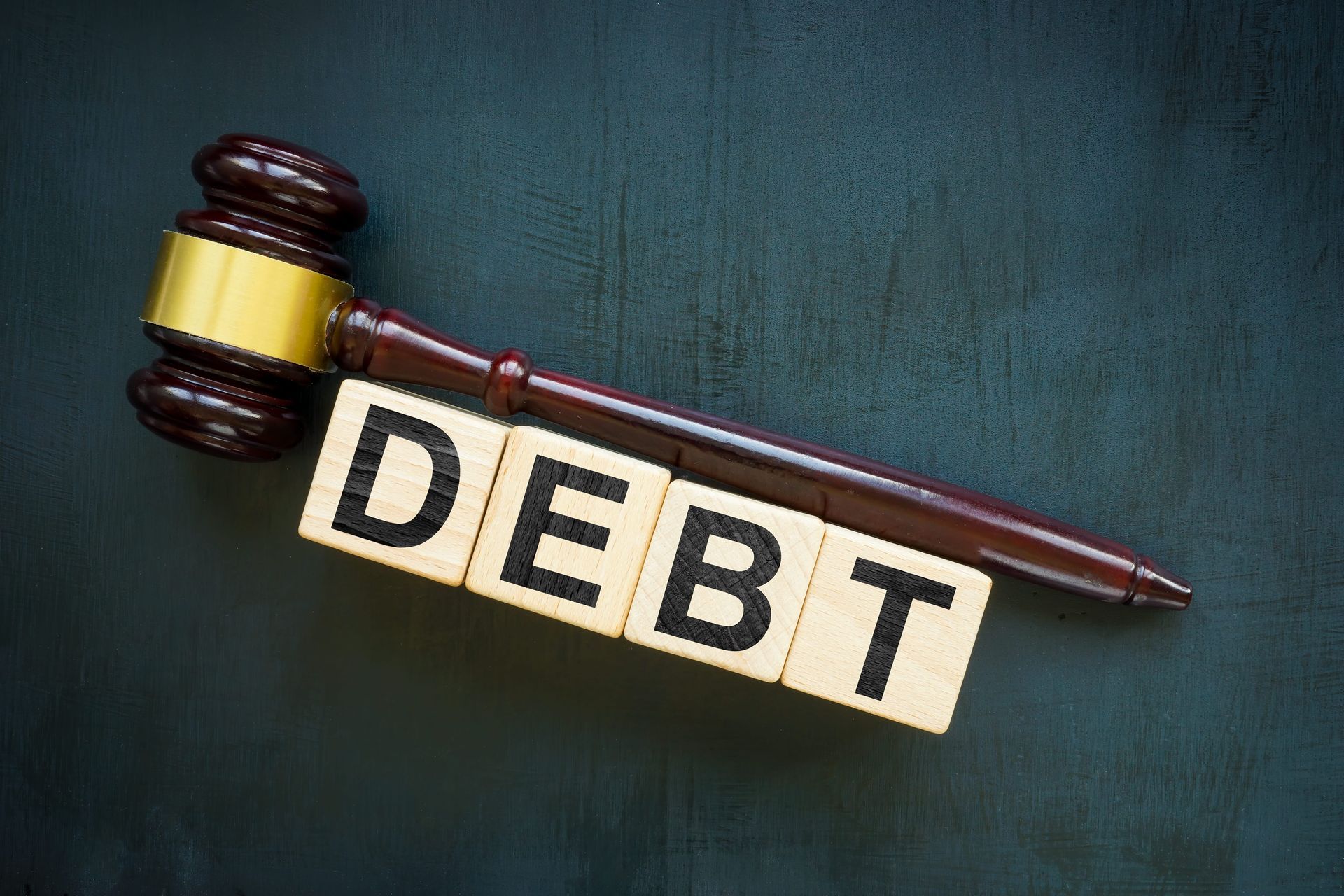 Judge’s gavel resting on tiles spelling “DEBT” against a dark background