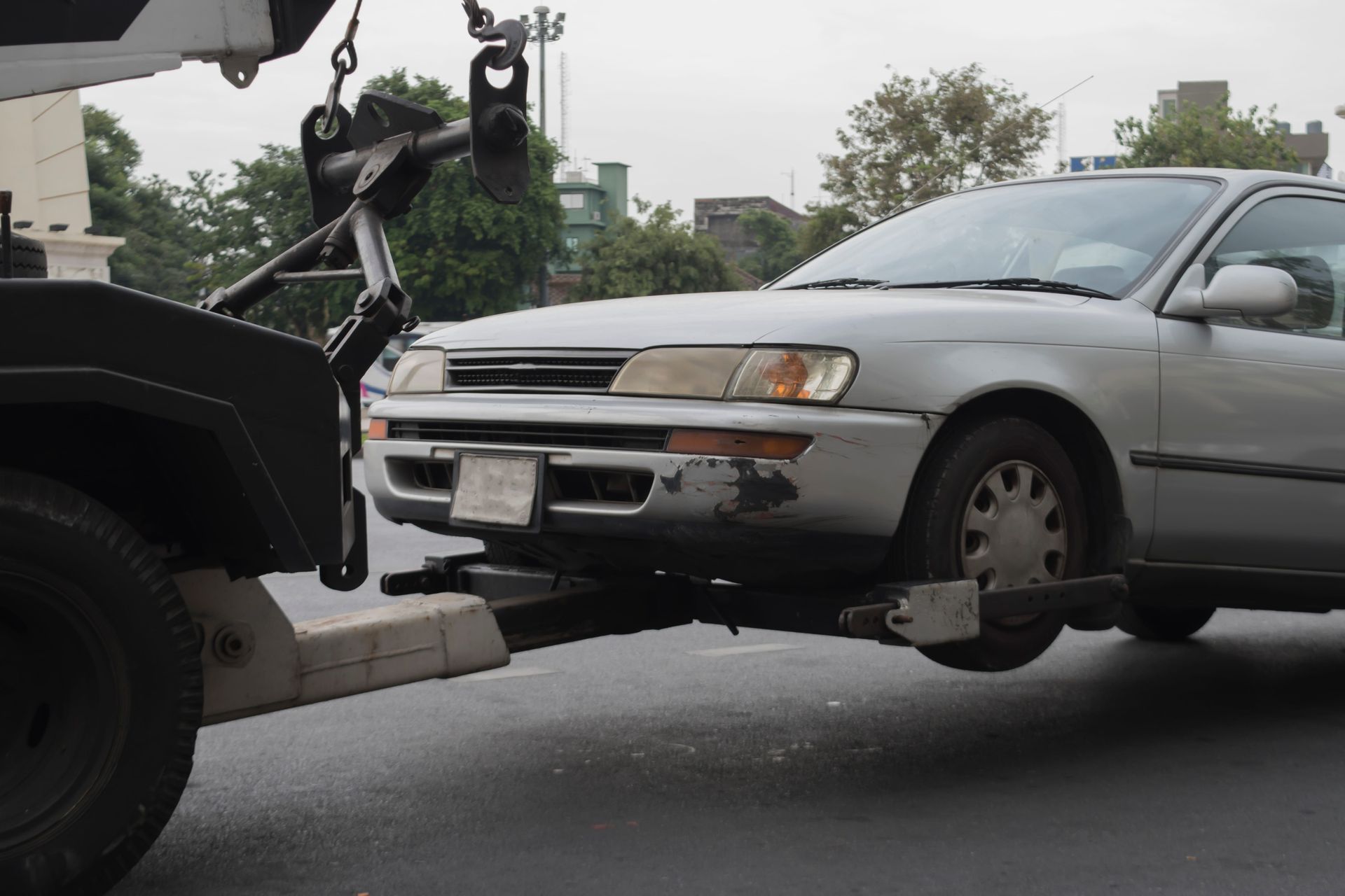 Silver car being towed by a tow truck on a city street.