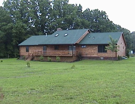 A brick house with a green roof sits in the middle of a grassy field