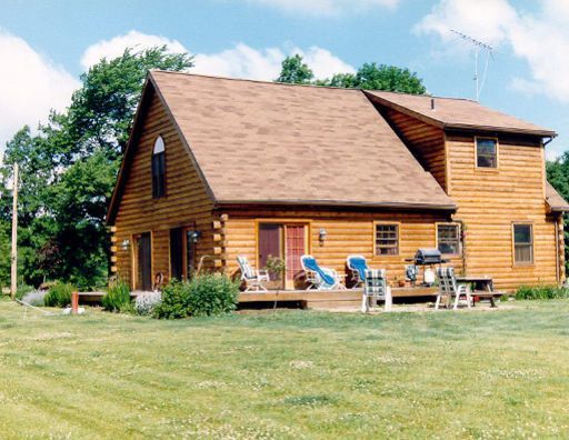 A large log cabin sits in the middle of a lush green field