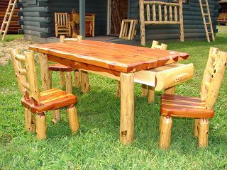 A wooden table and chairs are sitting in the grass in front of a log cabin.