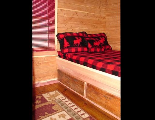 A bed with red and black plaid sheets and pillows in a cabin.