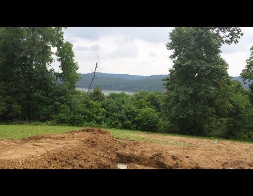 A dirt field with trees and a lake in the background