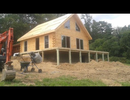 A large log cabin is being built in the middle of a dirt field.