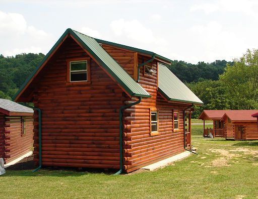 A log cabin with a green roof is sitting in the middle of a grassy field.