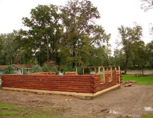 A log cabin is being built in a field with trees in the background