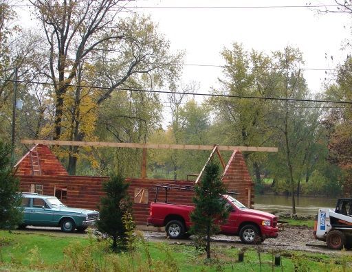 A red truck is parked in front of a log cabin under construction